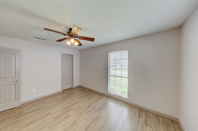 spare room featuring visible vents, light wood-style flooring, a ceiling fan, a textured ceiling, and baseboards