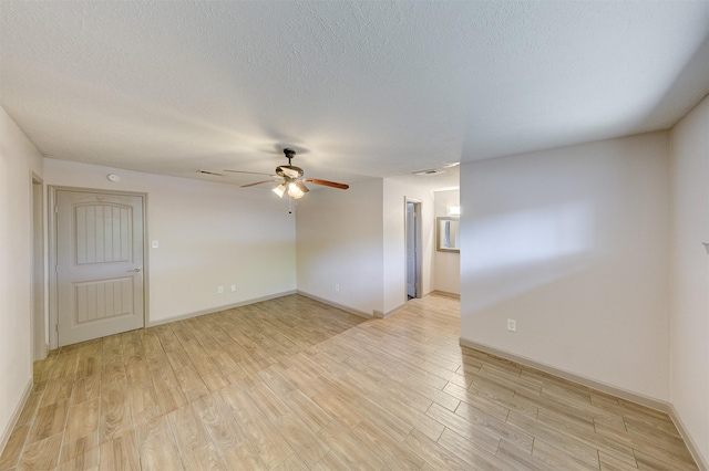 empty room with a ceiling fan, baseboards, a textured ceiling, and light wood finished floors