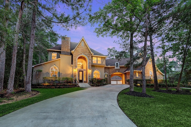 view of front of property with driveway, stone siding, a chimney, a front yard, and stucco siding