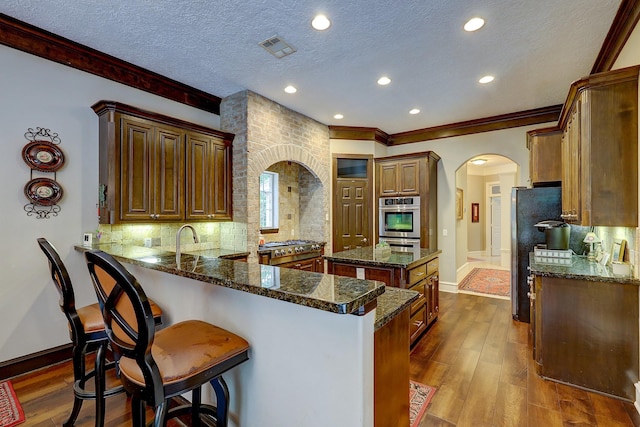 37314 Edgewater Dr, Pinehurst, TX 77362 - kitchen featuring arched walkways, crown molding, a peninsula, decorative backsplash, and dark stone countertops
