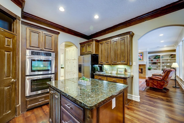 37314 Edgewater Dr, Pinehurst, TX 77362 - kitchen featuring stainless steel appliances, arched walkways, ornamental molding, dark wood-style floors, and dark stone countertops