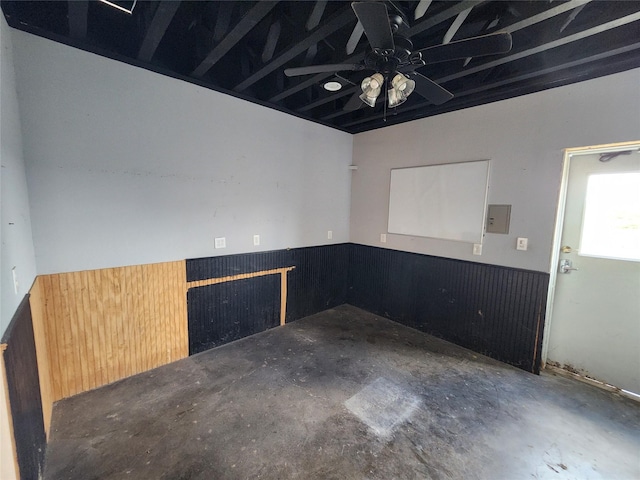 empty room with wainscoting, a ceiling fan, and electric panel