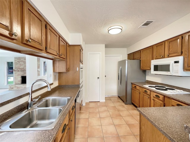 kitchen featuring light tile patterned floors, visible vents, brown cabinetry, stainless steel appliances, and a sink