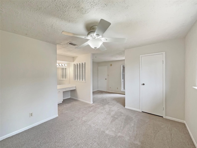 unfurnished bedroom with light carpet, baseboards, visible vents, a textured ceiling, and built in desk