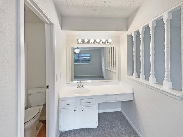 bathroom with a textured ceiling, vanity, toilet, and baseboards