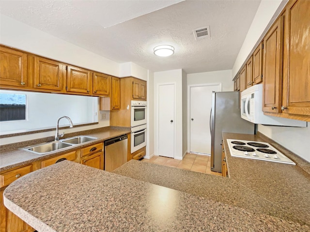 kitchen with white appliances, brown cabinetry, a sink, and visible vents