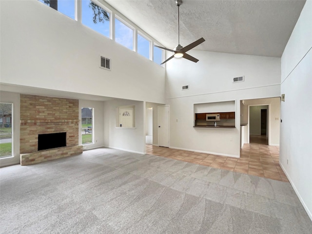 unfurnished living room with light carpet, visible vents, ceiling fan, a textured ceiling, and a fireplace