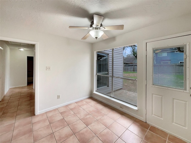 empty room featuring ceiling fan, a textured ceiling, light tile patterned flooring, and baseboards