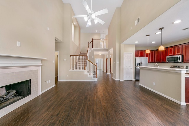 unfurnished living room featuring dark wood-type flooring, a brick fireplace, visible vents, and stairs