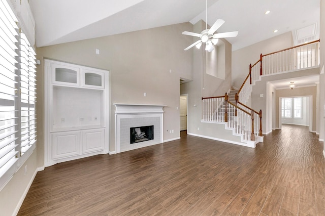 unfurnished living room featuring a ceiling fan, stairway, wood finished floors, a fireplace, and high vaulted ceiling