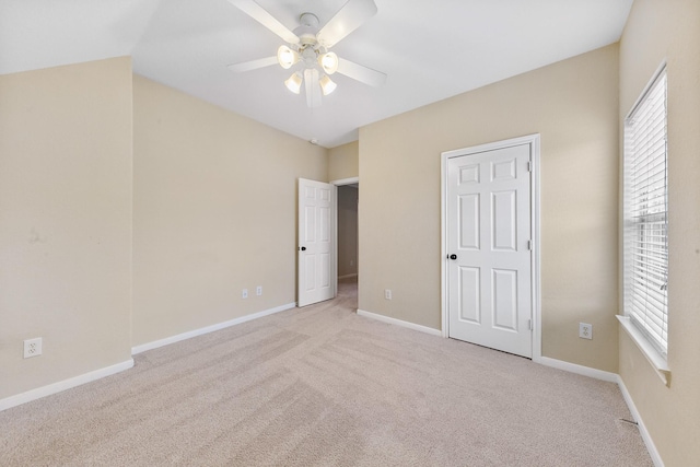 unfurnished bedroom featuring a ceiling fan, lofted ceiling, light colored carpet, and baseboards