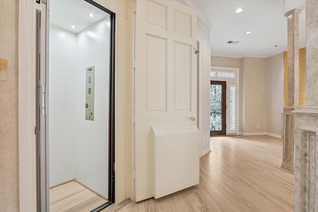 hall featuring baseboards, visible vents, elevator, ornate columns, and light wood-style floors