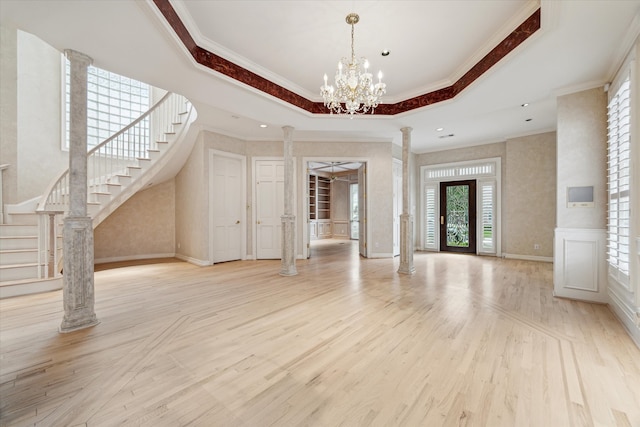 interior space with decorative columns, wood finished floors, stairs, a tray ceiling, and crown molding