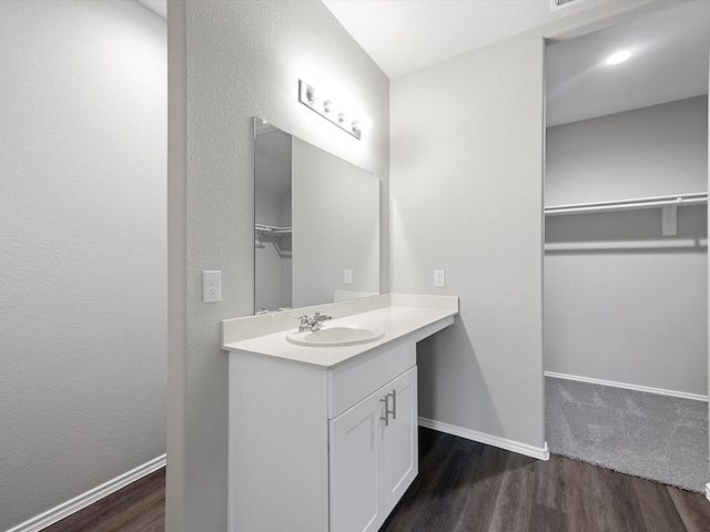 bathroom with a spacious closet, wood finished floors, vanity, and baseboards