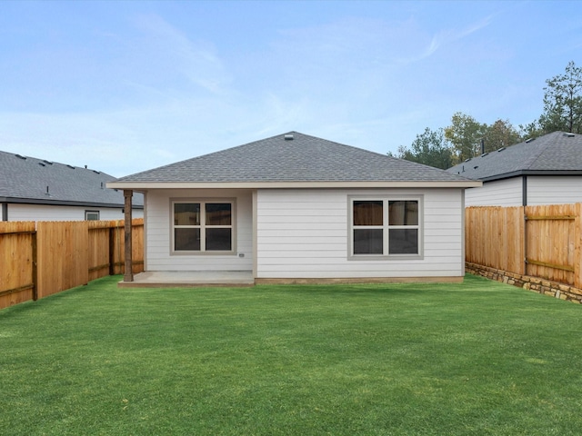 back of house with a fenced backyard, a shingled roof, and a lawn