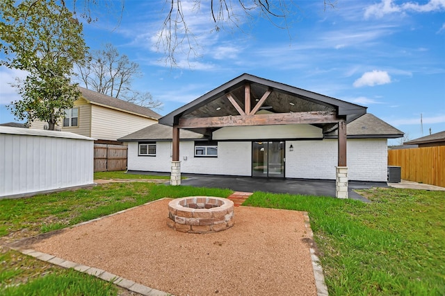 back of property with an outbuilding, a fire pit, fence, a lawn, and a patio area