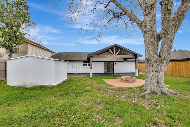 rear view of house featuring a fire pit, an outdoor structure, fence, a lawn, and a shed