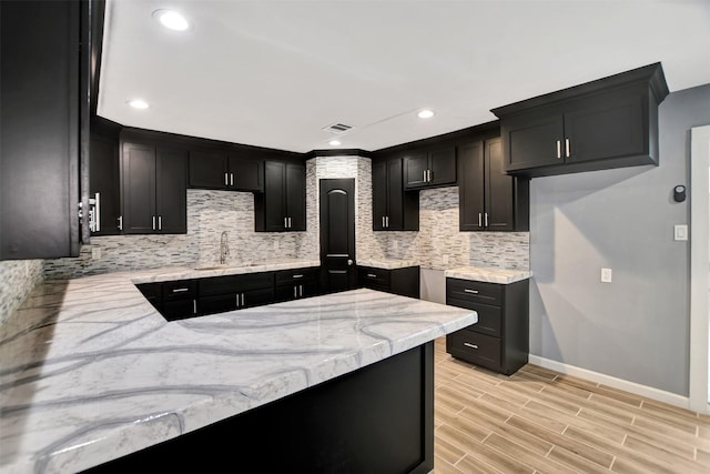 kitchen with wood finish floors, a sink, visible vents, decorative backsplash, and light stone countertops