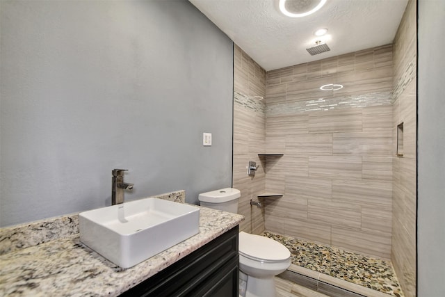 bathroom with a textured ceiling, vanity, a tile shower, and toilet