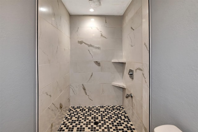 full bath featuring toilet, a textured wall, tiled shower, and visible vents