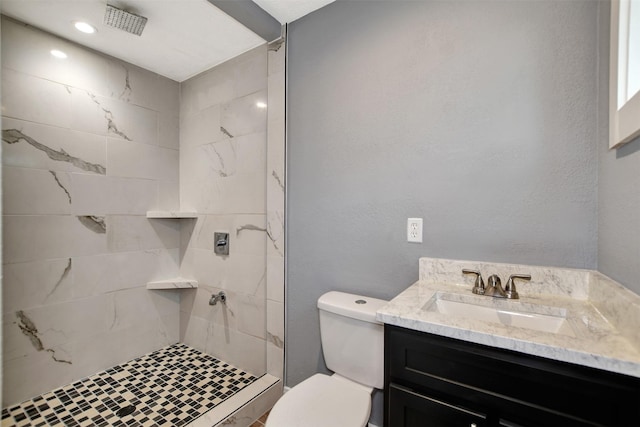 bathroom featuring a textured wall, vanity, a tile shower, and toilet