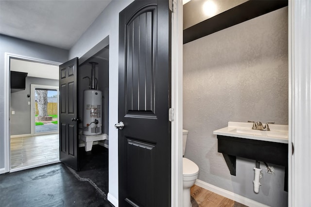 half bathroom with baseboards, gas water heater, toilet, wood finished floors, and a sink