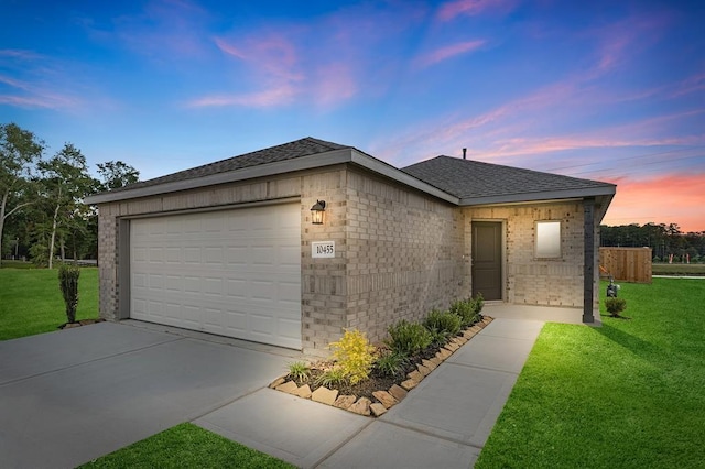 ranch-style house featuring a shingled roof, concrete driveway, an attached garage, a yard, and brick siding