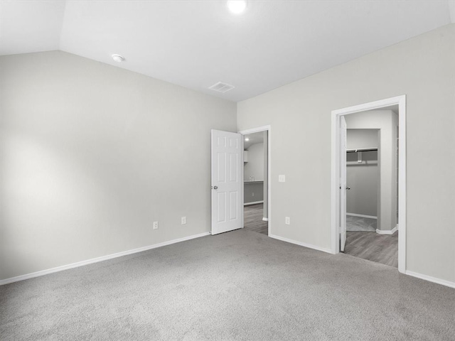 unfurnished bedroom featuring carpet floors, a walk in closet, lofted ceiling, visible vents, and baseboards