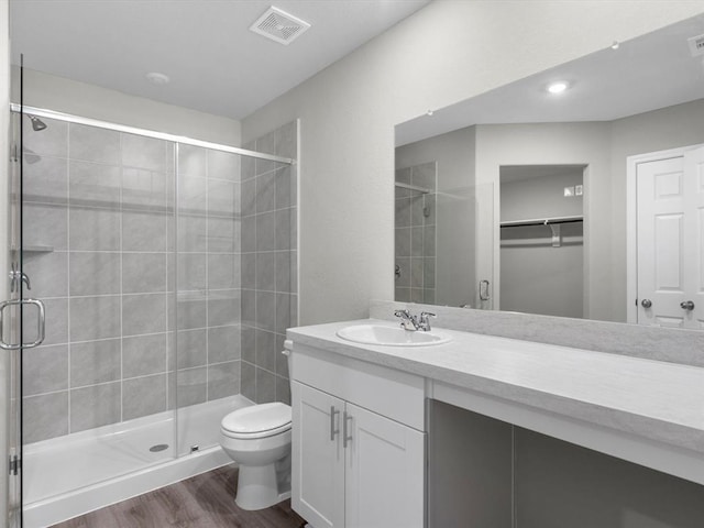 full bathroom with visible vents, toilet, vanity, a shower stall, and wood finished floors