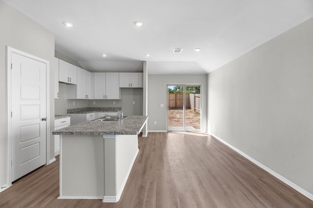 kitchen with visible vents, white cabinets, an island with sink, wood finished floors, and a sink