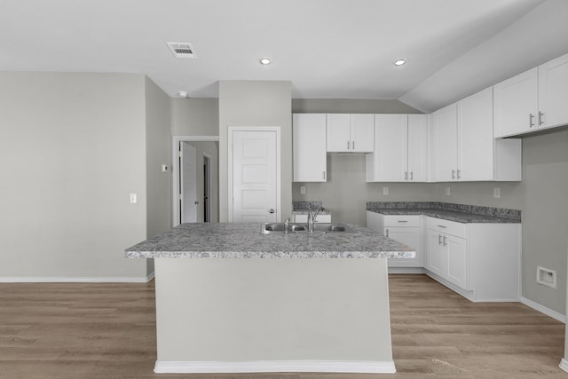 kitchen with light wood finished floors, a center island with sink, baseboards, white cabinetry, and a sink