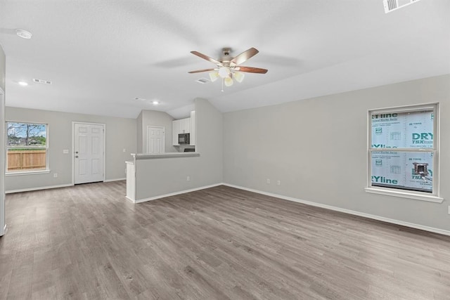 unfurnished living room featuring ceiling fan, light wood-style flooring, visible vents, baseboards, and vaulted ceiling