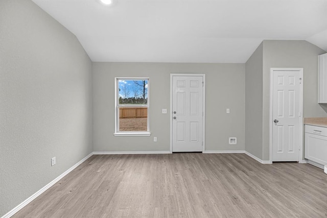 interior space with light wood-type flooring, vaulted ceiling, and baseboards