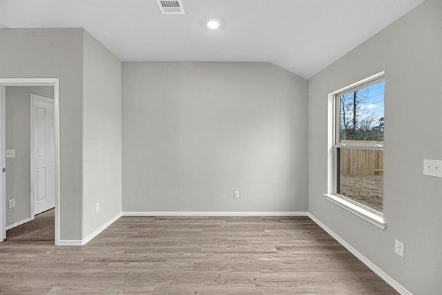 spare room featuring lofted ceiling, wood finished floors, visible vents, and baseboards