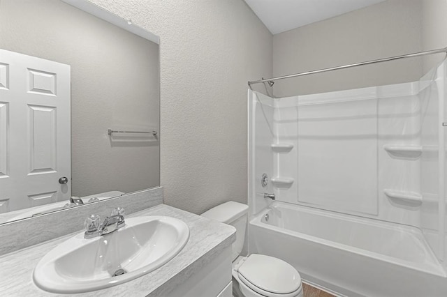 full bath featuring bathtub / shower combination, a textured wall, vanity, and toilet