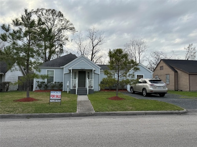 bungalow-style home featuring a shingled roof, a front yard, and driveway