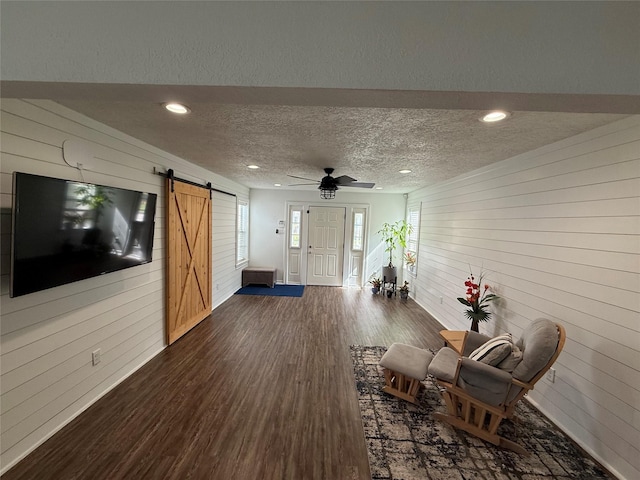 interior space with a textured ceiling, a barn door, dark wood-style flooring, and wooden walls