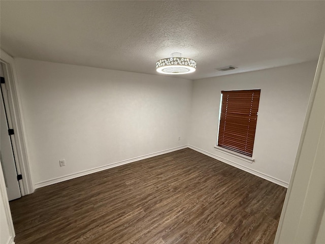 unfurnished room with baseboards, visible vents, dark wood finished floors, and a textured ceiling