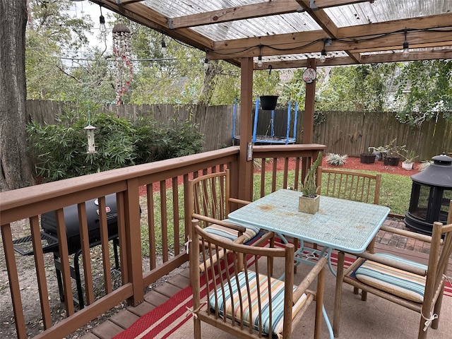 wooden deck with a trampoline, outdoor dining area, and a fenced backyard