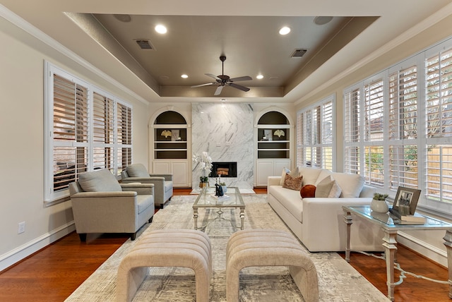 living room with a tray ceiling, built in shelves, visible vents, and wood finished floors