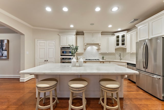 kitchen featuring stainless steel appliances, wood finished floors, a kitchen island, a sink, and visible vents