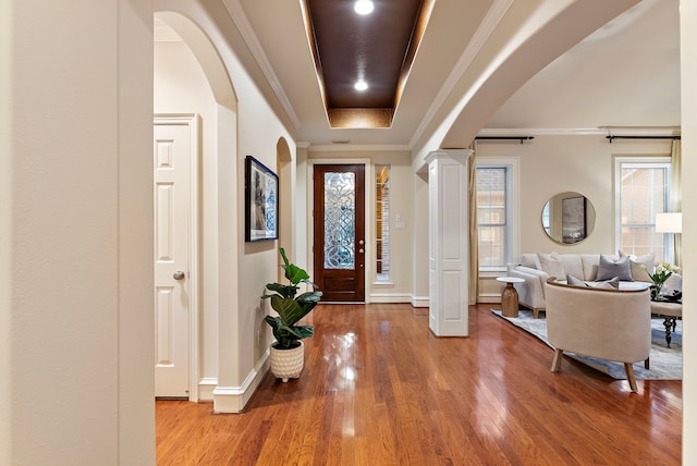 entryway with ornate columns, arched walkways, hardwood / wood-style flooring, crown molding, and a raised ceiling