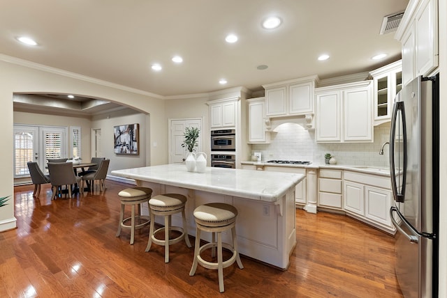 kitchen with arched walkways, dark wood-style floors, ornamental molding, appliances with stainless steel finishes, and a center island