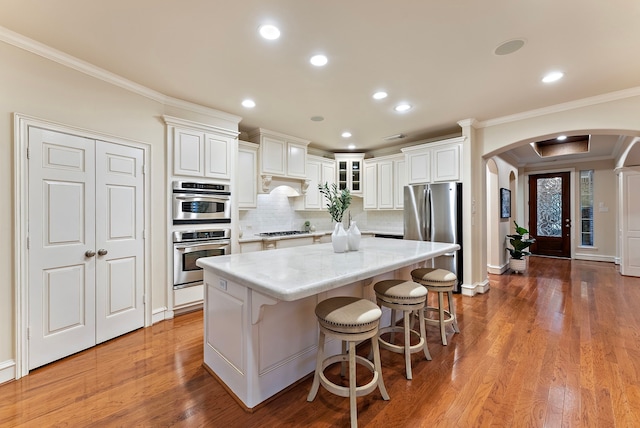 kitchen with appliances with stainless steel finishes, arched walkways, a center island, and crown molding