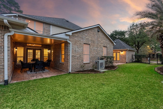 back of property at dusk with ac unit, fence, a lawn, and brick siding