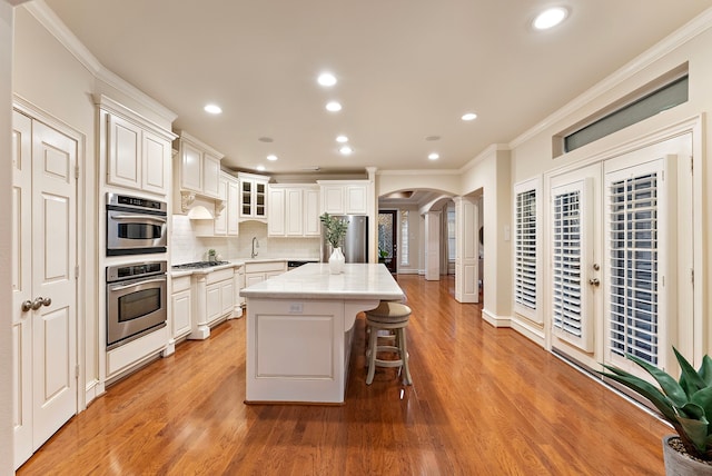 kitchen with arched walkways, appliances with stainless steel finishes, a center island, a kitchen bar, and backsplash