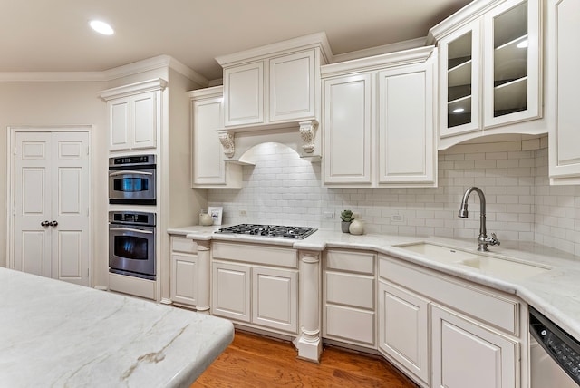 kitchen with decorative backsplash, appliances with stainless steel finishes, ornamental molding, light wood-type flooring, and a sink