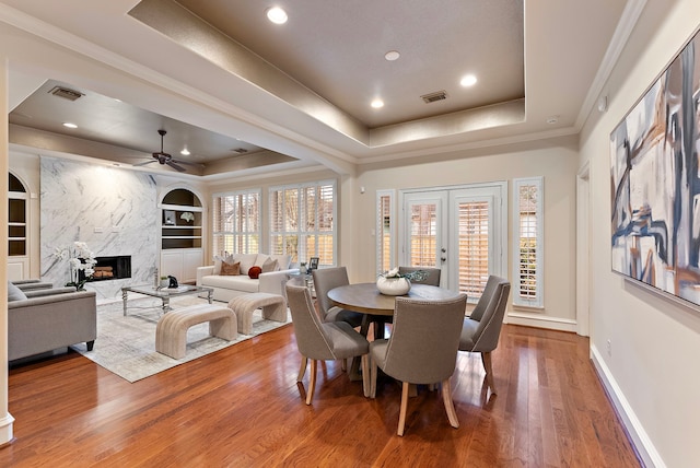 dining space featuring a tray ceiling, visible vents, a fireplace, and wood finished floors