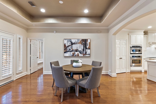 dining area with a tray ceiling, arched walkways, crown molding, light wood finished floors, and visible vents