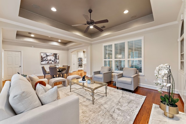 living room with a raised ceiling, a ceiling fan, wood finished floors, arched walkways, and baseboards